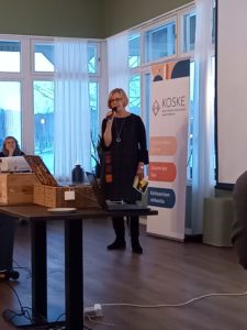 Kuvassa Kosken johtaja Sointu Möller kiittämässä yleisön edessä mikrofoniin puhuen työntekijöitä, yhteistyökumppaneita ja vapaaehtoisia.
